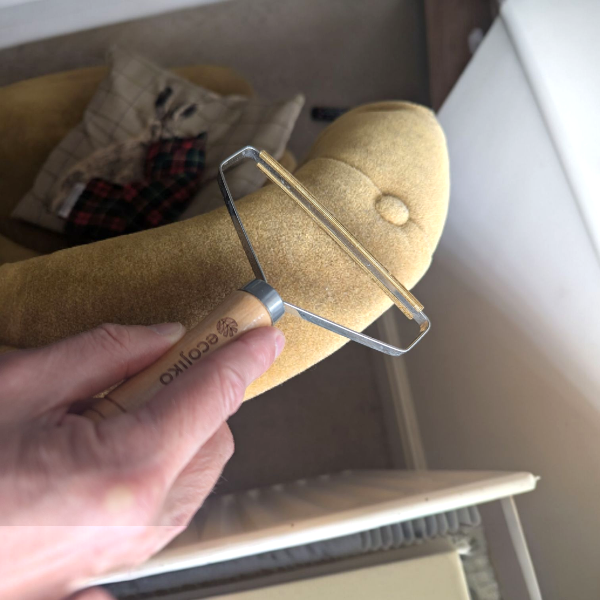 Wooden-handled metal tool lint and hair remover in use on upholstery