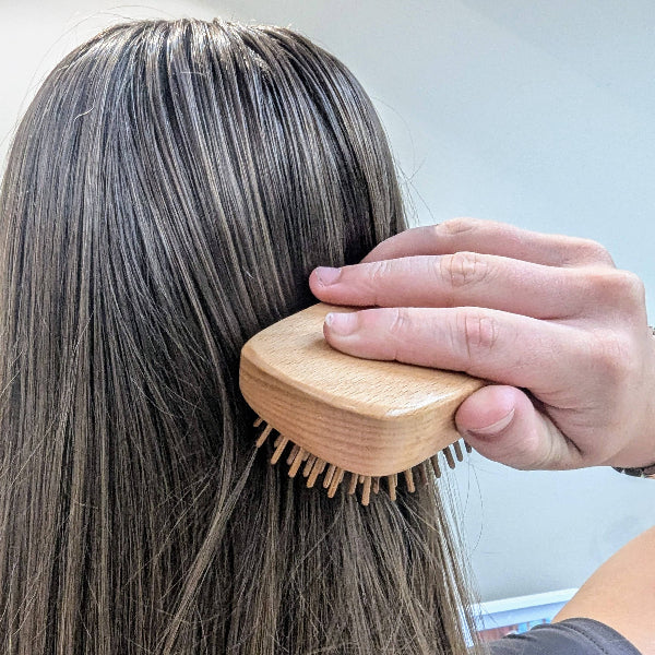 Person brushing long hair with wooden detangling brush against a light background