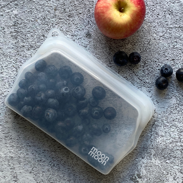 Silicone food pouch containing blueberries and an apple on a grey surface