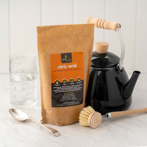 Natural citric acid in kraft paper poch shown next to a wooden dish brush, black kettle, measuring and spoon