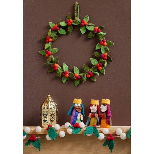 Felt berry wreath with green felt leaves and red felt berries, hanging on a wall with a felt nativity set