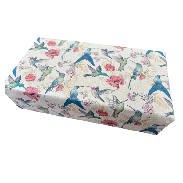 Planetwrapit eco-friendly wrapping paper shown on a wrapped parcel, featuring a pattern of blue hummingbirds, pink flowers, and green leaves on a brown kraft paper background.