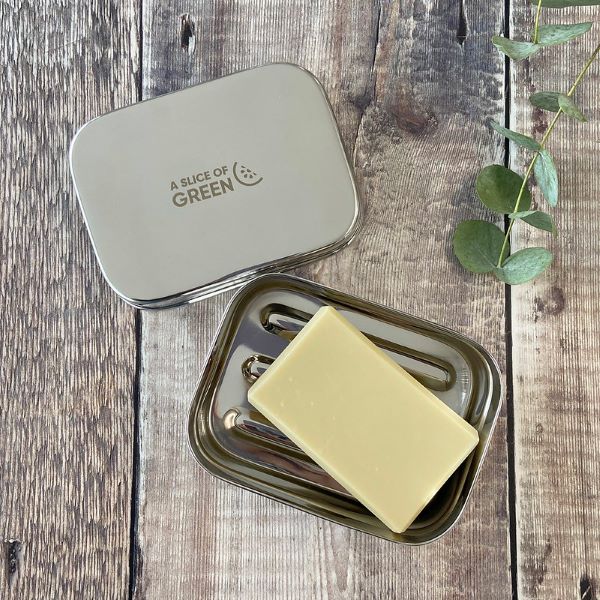 Travel soap or snack tin with lid shown off to see ridged base inside with a bar of soap laying inside. Lid has logo reading A Slice of Green.