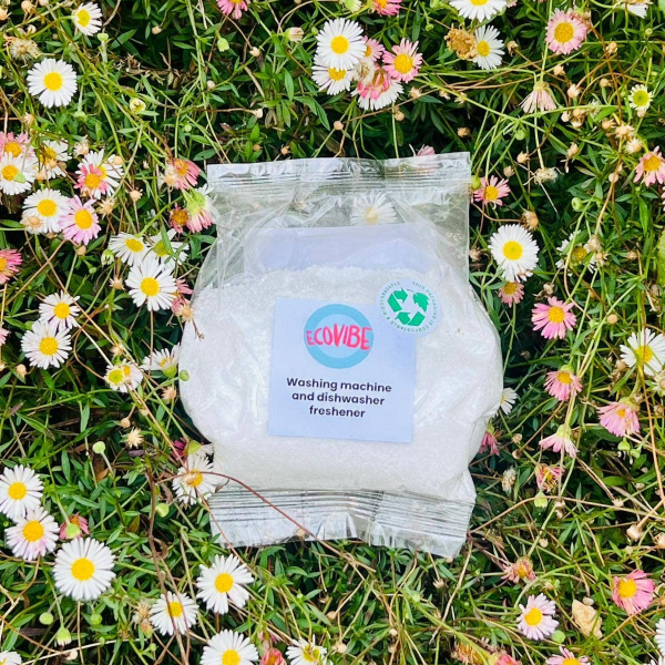 EcoVibe washing machine and dishwasher cleaner in eco-friendly packaging lying on grass and wild flowers