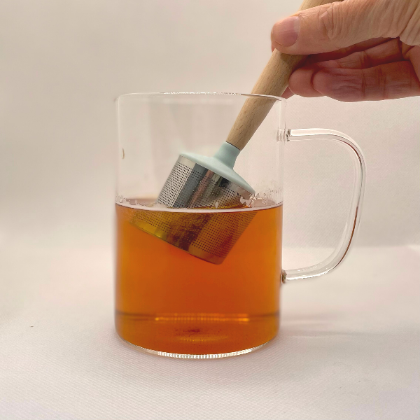 Clear glass mug with Dunker tea strainer being dipped inside making tea