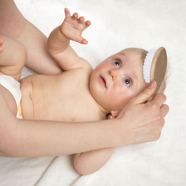 Baby with a nappy having hair brushed with a bamboo hairbrush