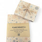 PlanetWrapIt recycled kraft wrapping paper in Christmas Snowflakes (brown paper with printed colourful snowflakes shown alongside wrapped parcel with gold ribbon