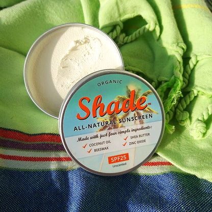 Tin of Shade all-natural sunscreen with a colourful label on a white background, shown in aluminium tin with lid off, on a blue and green fabric