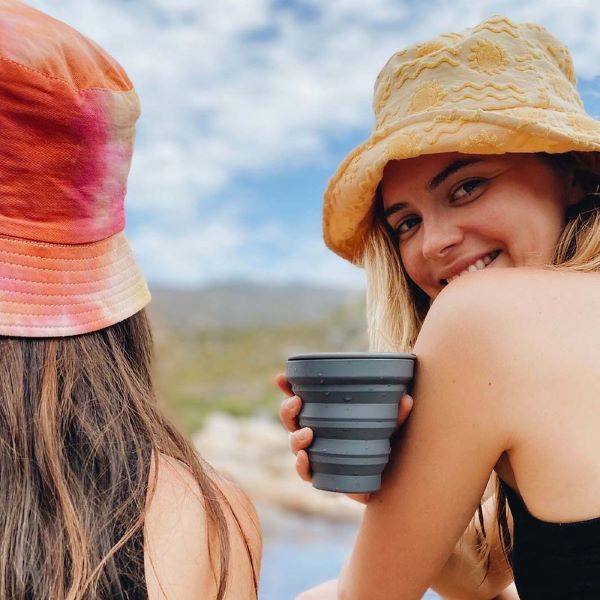Collapsible cup shown in charcoal in the hand of a girl on a beach
