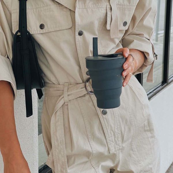 Collapsible cup 16oz shown in charcoal with flexible straw in the hand of a person out and about