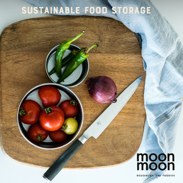 Wooden cutting board with storage pots containing tomatoes, green peppers, an onion, alongside a knife on a white background with 'moon moon' branding.