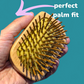 Hand holding a wooden detangling hairbrush with text 'perfect palm fit' on a teal background