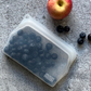 Silicone food pouch containing  blueberries and an apple on a grey surface