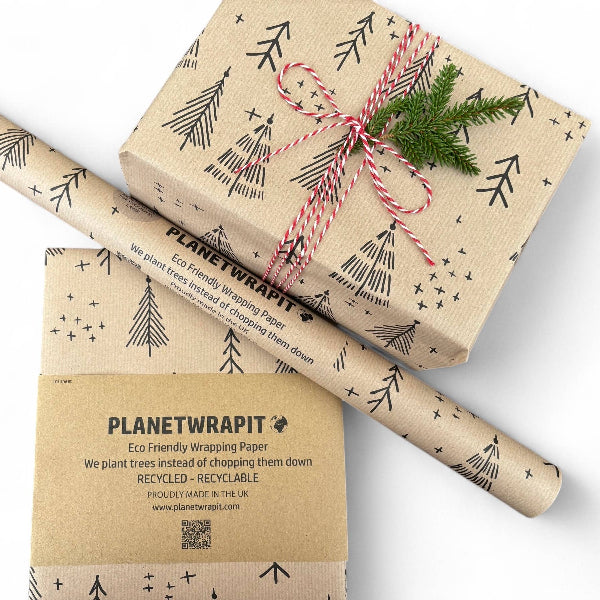 PlanetWrapIt recycled kraft wrapping paper in Christmas trees black (brown paper with printed black Christmas trees) shown alongside wrapped parcel with red twine and natural foliage