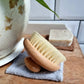 Wooden body brush on a towel with soap in the background