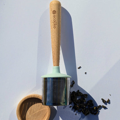 Dunker tea strainer with wooden handle and metal strainer on a white  background with tea leaves