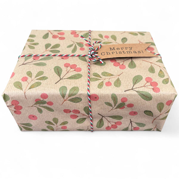 PlanetWrapIt recycled kraft wrapping paper in Christmas mistletoe (brown paper with printed red berries and green leaves) shown on a wrapped parcel with colourful twine and a paper label reading 'Merry Christmas'