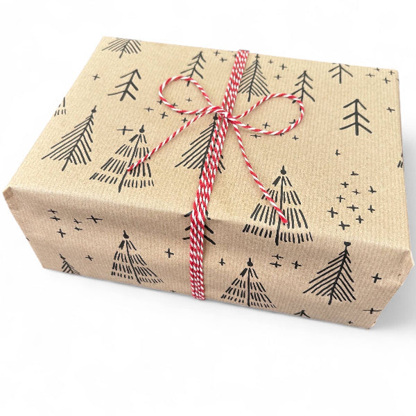 PlanetWrapIt recycled kraft wrapping paper in Christmas trees black (brown paper with printed black Christmas trees) shown on wrapped parcel with red twine