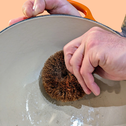 Person scrubbing a pot with hedgehog coconut fibre scrubber in a sink