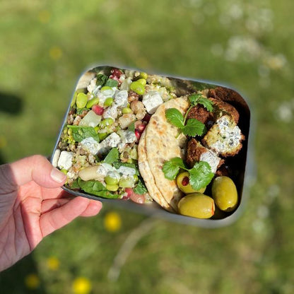 Hand holding Adoni stainless steel lunchbox with lid off showing food inside