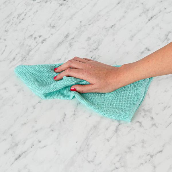 Hand holding an all-purpose cloth on a marble surface