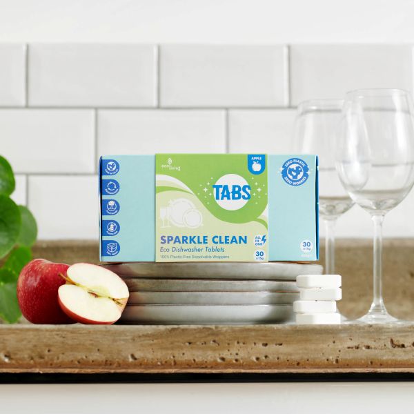Box of Sparkle Clean dishwasher tablets on a kitchen counter with apples and glasses.