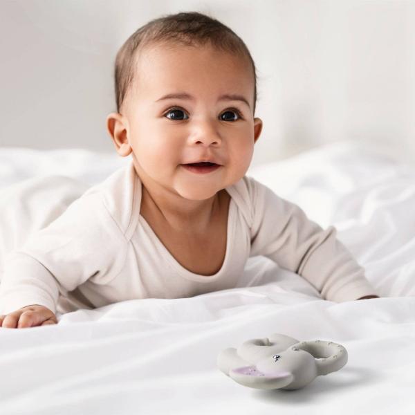 Baby lying on a white blanket with elephant teething toy nearby