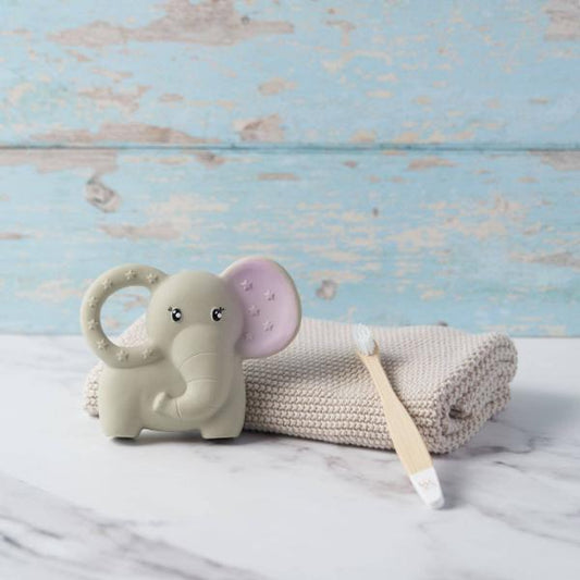 An elephant-shaped baby teether in a warm off-white colour, shown next to a knitted hand towel and baby toothbrush