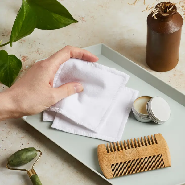 Cotton make up squares shown in a hand next to a comb and small pot cream
