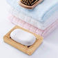 Bamboo soapdish shown holding a white bar of soap next to some towels and a hairbrush
