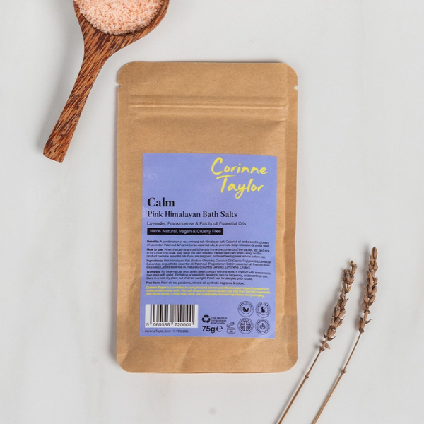 A kraft paper pouch of Corinne Taylor Calm Pink Himalayan Bath Salts, on a white background with a wooden spoon of pink bath salt crystals and dried lavender sprigs.