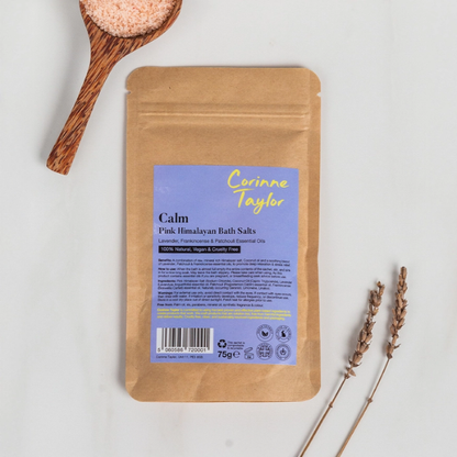 A kraft paper pouch of Corinne Taylor Calm Pink Himalayan Bath Salts, on a white background with a wooden spoon of pink bath salt crystals and dried lavender sprigs.
