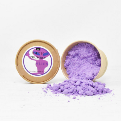 Bain and Savon bath crumble in Unicorn dust shown in paper pot with lid of and purple bath crumble inside