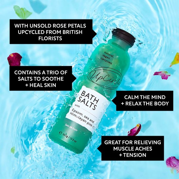 UpCircle bath salts in glass bottle on water background and rose petals, with text reading "with unsold rose petals upcycled from British florists, contains a trio of salts to soother and heal skin, calm the mind and relax the body, great for relieving muscle aches and tension"