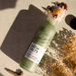 Glass bottle of UpCircle Bath Salts on a textured surface with dried flowers and leaves.