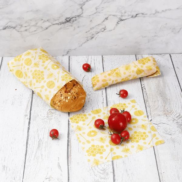 Yellow beeswax wrap with bread and tomatoes on a wooden surface