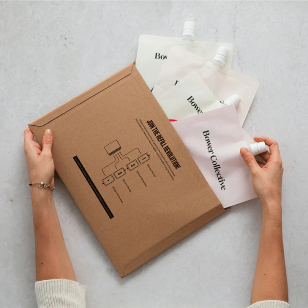 Person popping Bower Collective empty refill pouches into cardboard envelope for return.