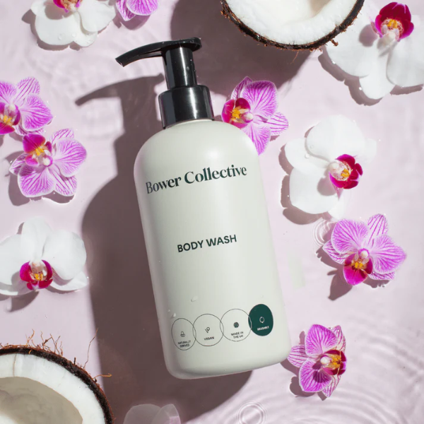 Bower Collective body wash dispenser bottle surrounded by pink orchids on a light pink background