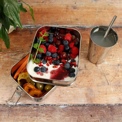 Buruni two-tier leak-resistant stainless steel lunchbox shown with yoghurt and fruit in top layer and a bagel in lower level alongside stainless steel cup and straw