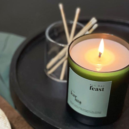 Clean-burning refillable mini Christmas candle in All Day Feast scent in a green glass jar, lit on a black plate