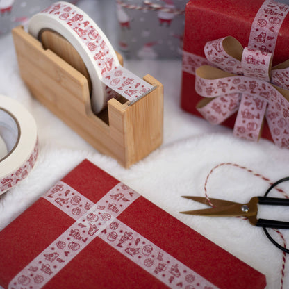 Red and white patterned paper tape displayed on a wooden tape dispenser, wrapped around gift boxes, with scissors on a white textured surface.