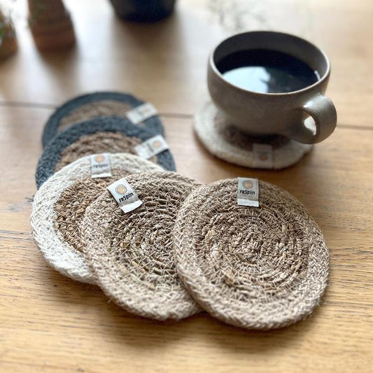 Set of 6 seagrass coasters with jute trim in natural tones next to a cup containing a hot drink