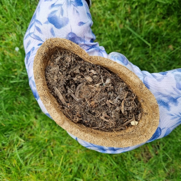 Coco coir biodegradable and reusable plant pot shown with compost inside being squeezed within gloved hands 
