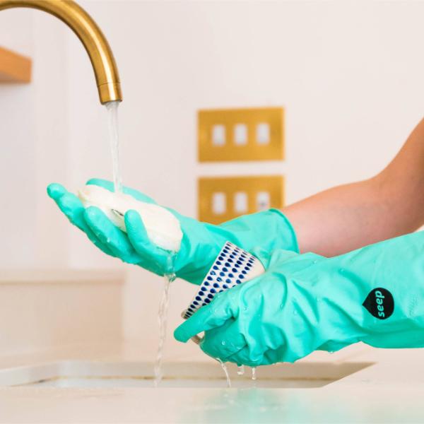 A person wearing rubber cleaning gloves washes a cup with a compostable sponge 