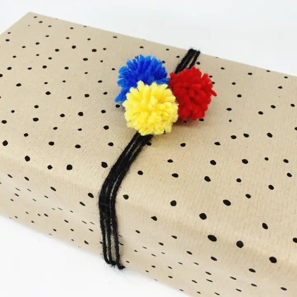 Eco-friendly wrapping paper from PlanetWrapit, brown kraft paper with little black dots, shown with woolly pompoms 