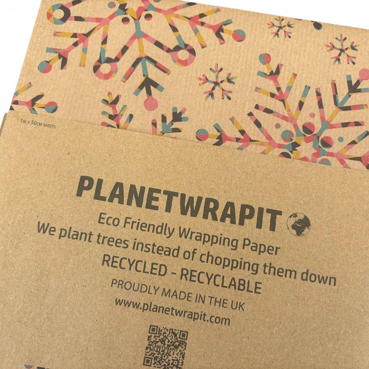 Planetwrapit eco-friendly wrapping paper shown in its kraft paper sleeve packaging, featuring colorful snowflake patterns on a brown background with product details printed on the front.
