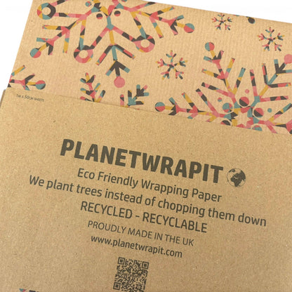 Planetwrapit eco-friendly wrapping paper shown in its kraft paper sleeve packaging, featuring colorful snowflake patterns on a brown background with product details printed on the front.