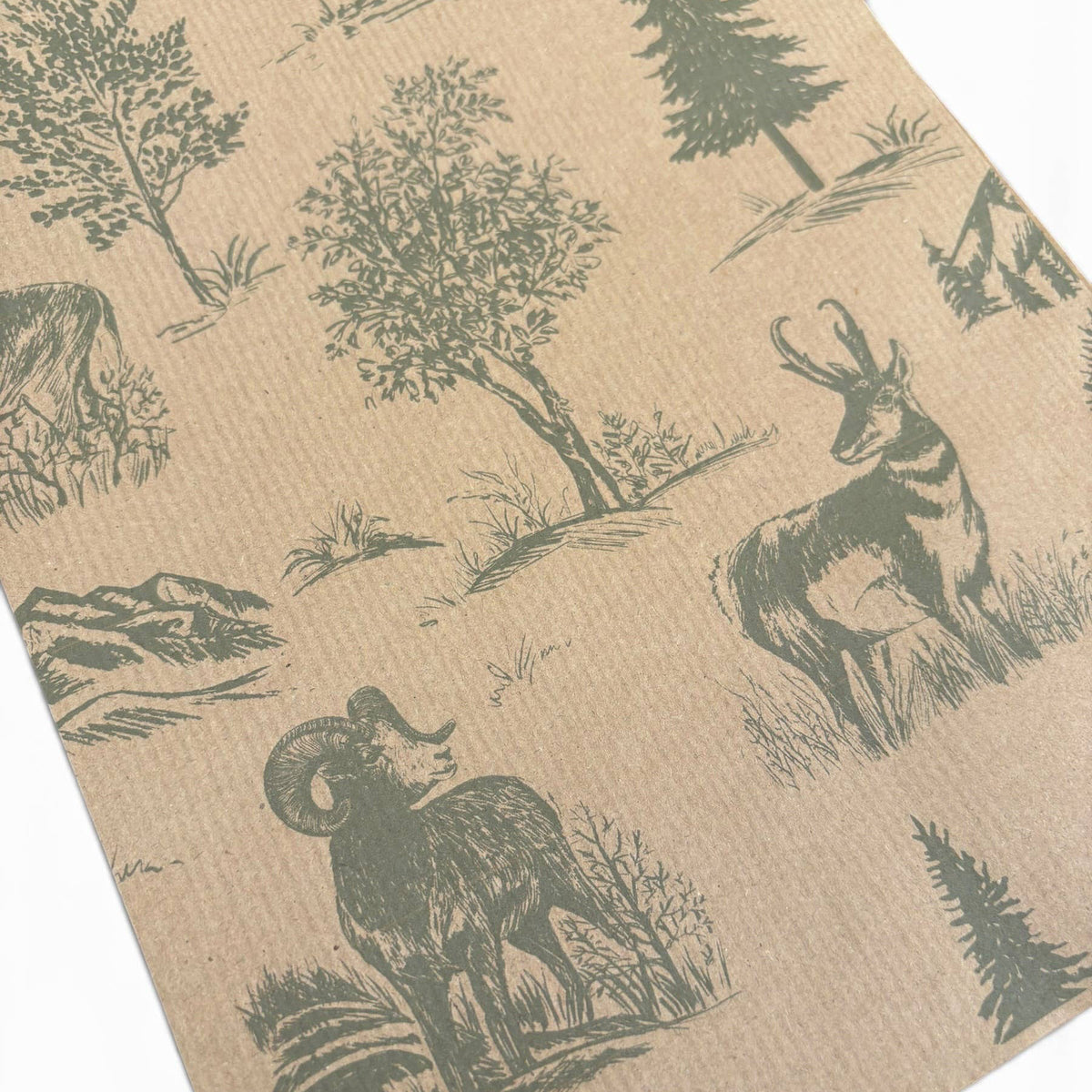 A close-up of a kraft paper surface printed with a repeating toile-style nature pattern featuring trees, shrubs, mountains, and animals including a ram and deer in dark olive green.