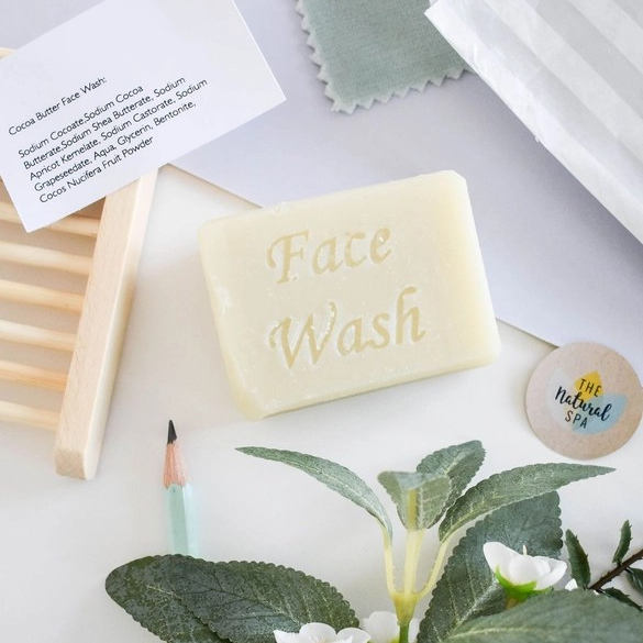 Facial soap bar (cocoa butter) shown with greenery and a wooden soapdish, the words 'Facial wash' stamped on the bar