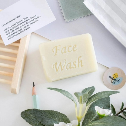 Facial soap bar (cocoa butter) shown with greenery and a wooden soapdish, the words 'Facial wash' stamped on the bar